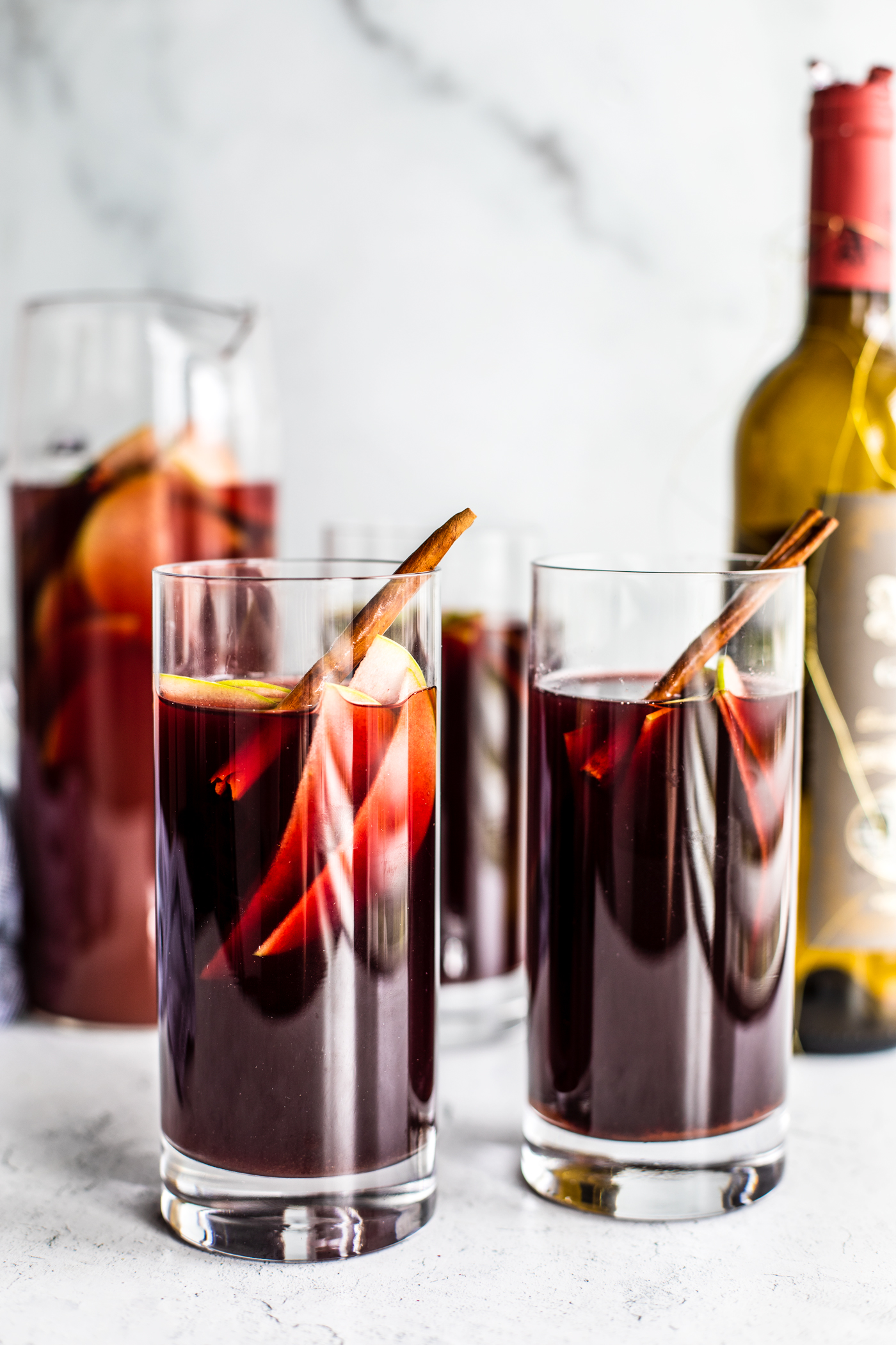 Two tall glasses of sangria with sliced green apples and cinnamon sticks in it.