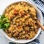 Serving bowl full of rice pilaf with a wooden spoon and blue and white striped hand towel underneath.