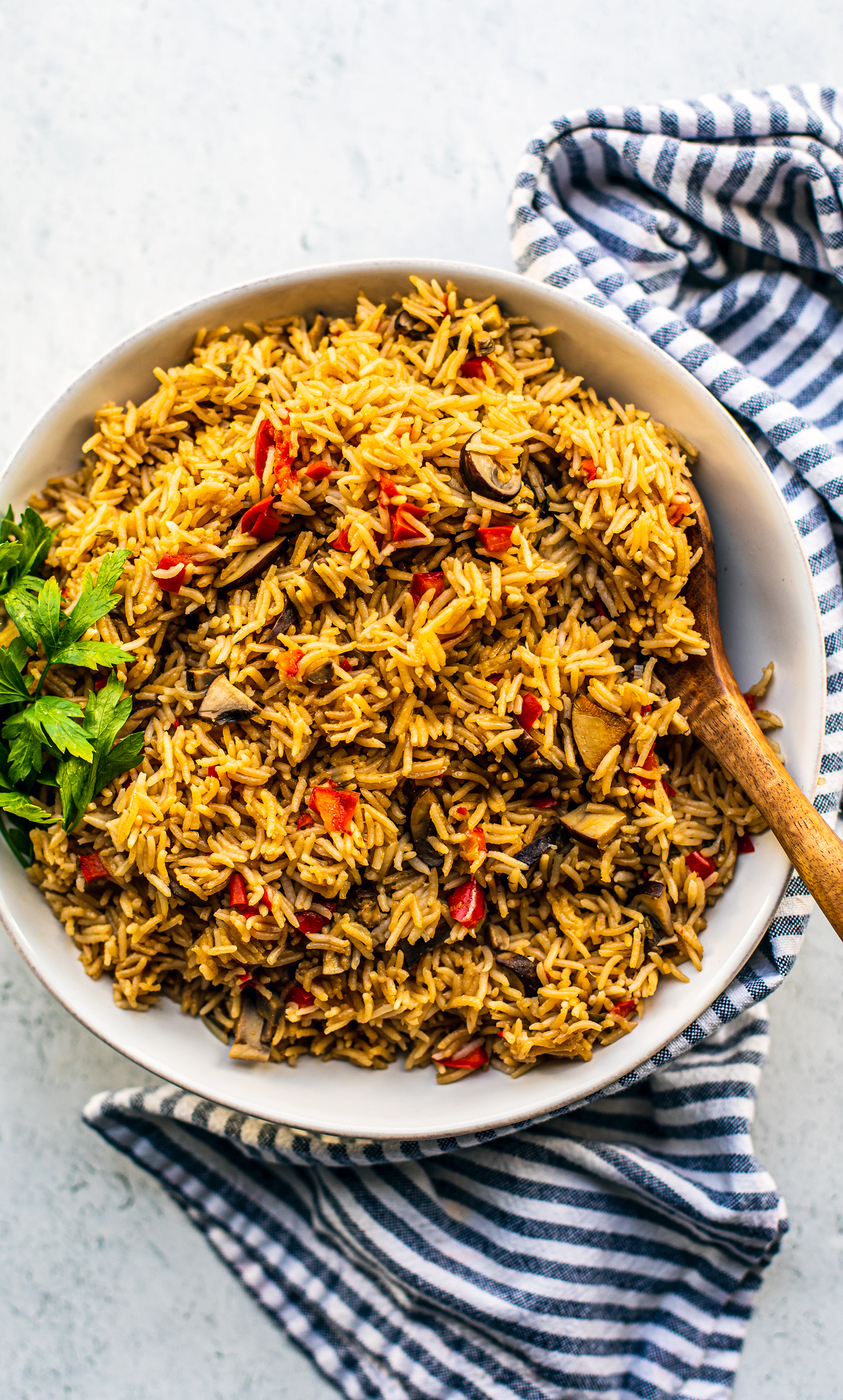 Serving bowl full of rice pilaf with a wooden spoon and blue and white striped hand towel underneath.