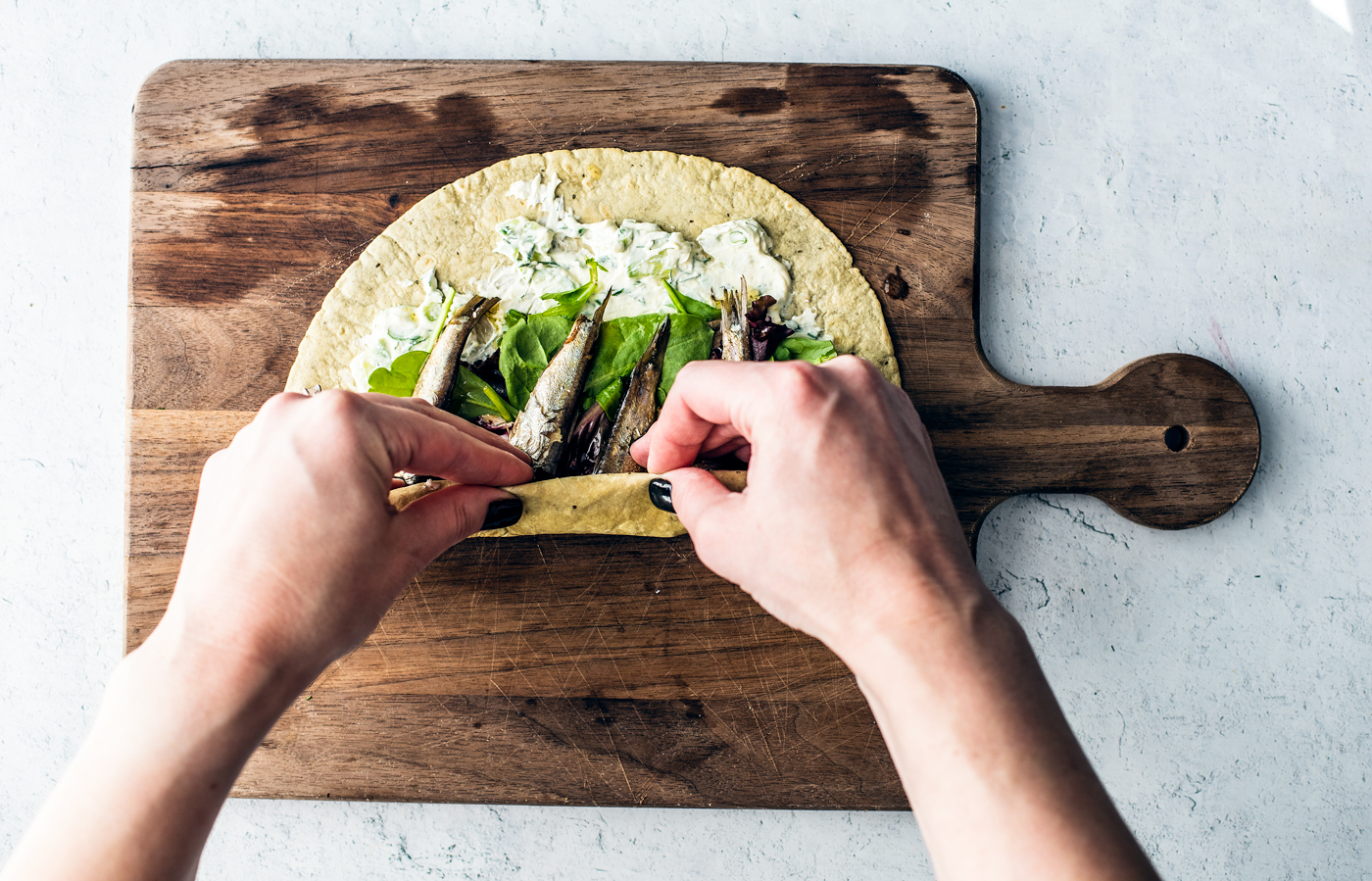 Hands rolling a tortilla, filled with greens and sardines, from the bottom up.