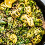 Close up of skillet full of ground sausage and tortellini with lemon slices on the side.