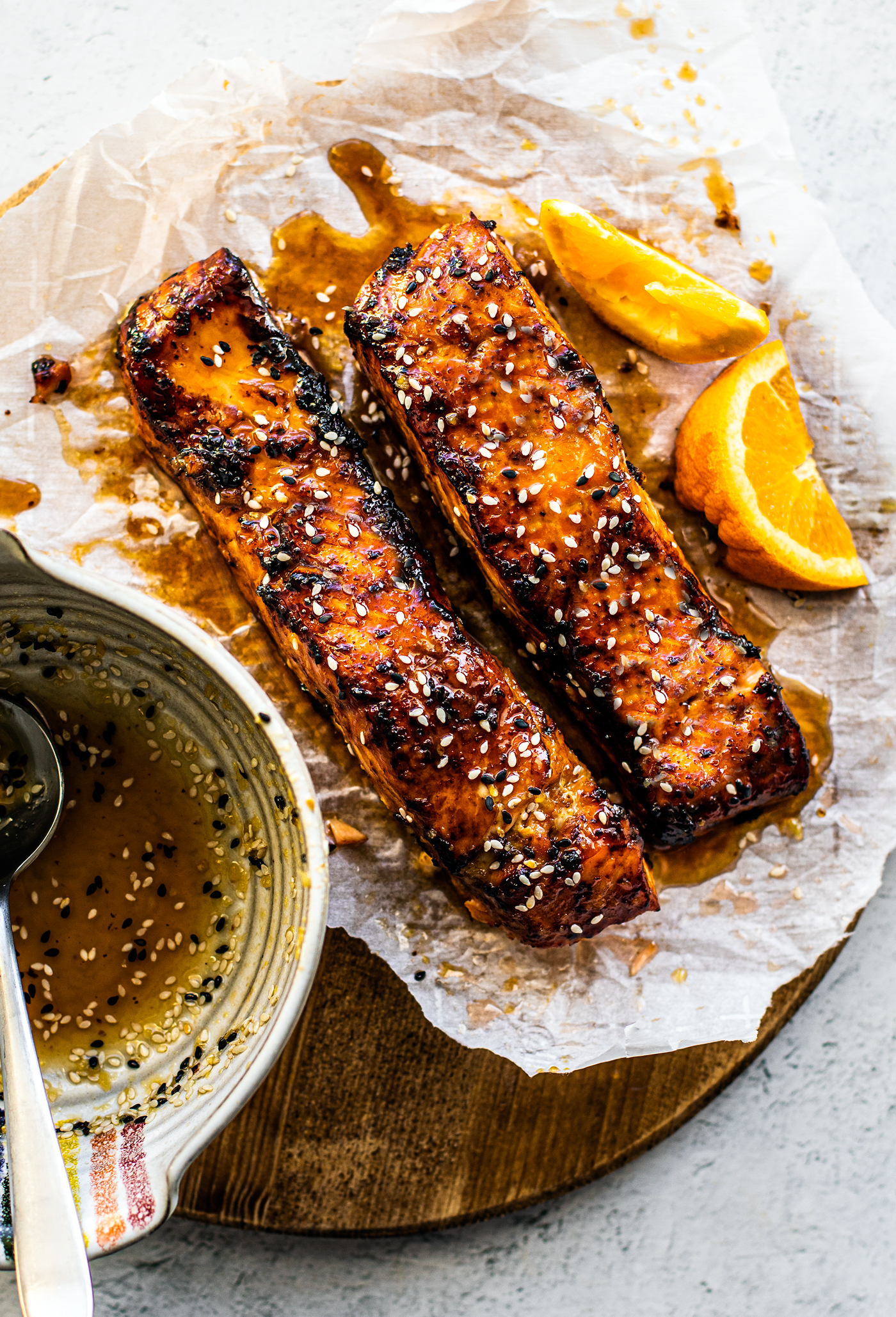 Caramelized salmon fillets on parchment over a cutting board with bowl of glaze next to it.