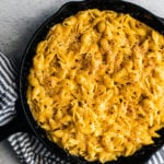 Baked homemade mac and cheese in a cast iron skillet with a kitchen towel wrapped around part of it.