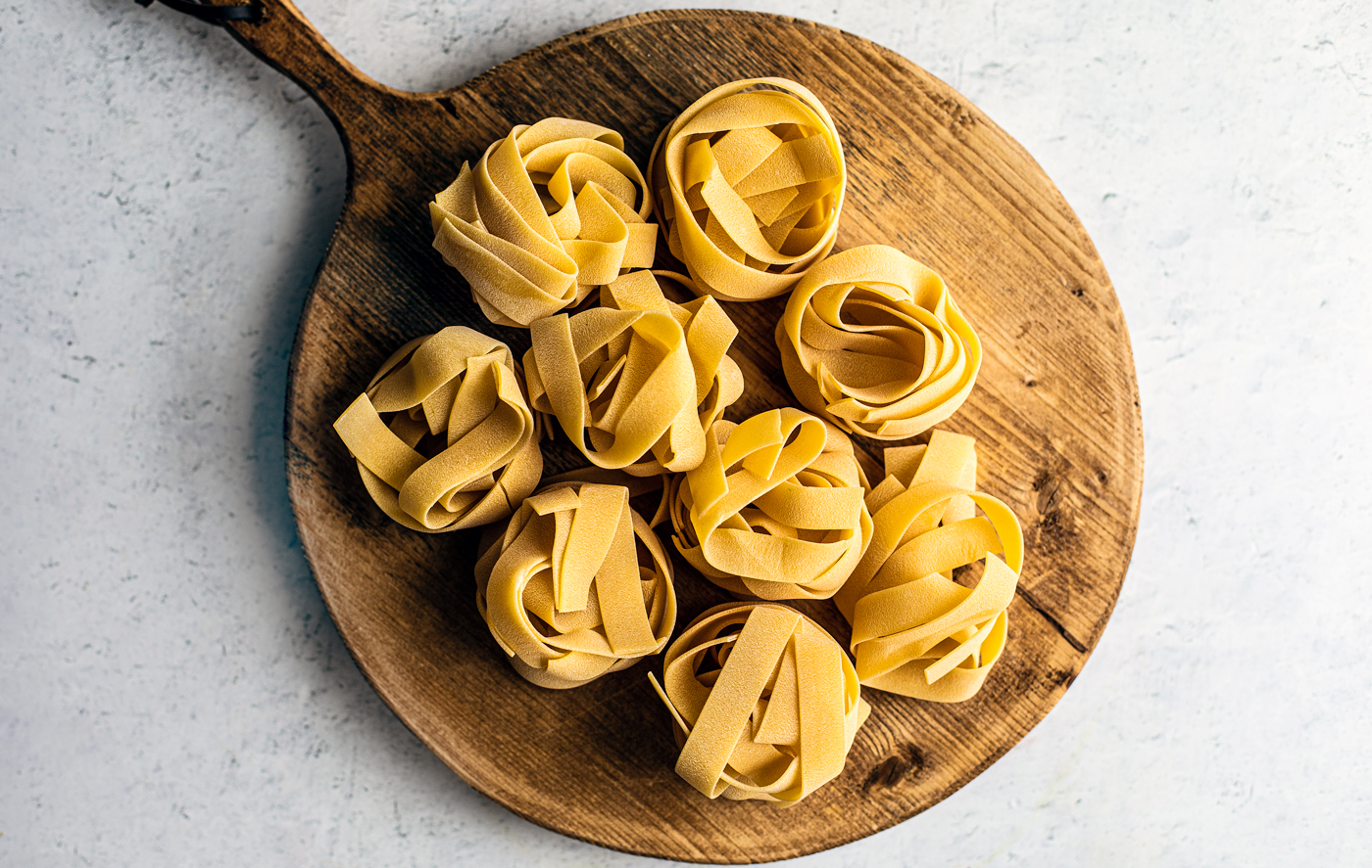 Nests of pappardelle pasta on a round wooden cutting board.
