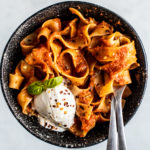 Black speckled bowl full of pappardelle and a scoop of burrata.
