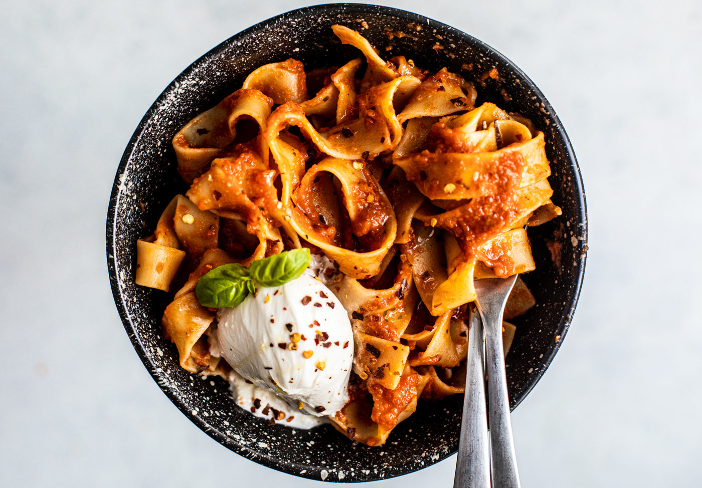 Black speckled bowl full of pappardelle and a scoop of burrata.