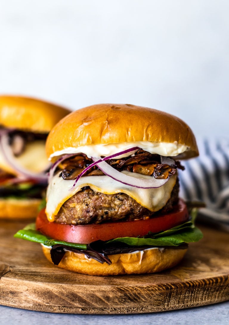 Close up shot of stacked turkey burger with greens, tomato slice, melted cheese, onions, and mushrooms.