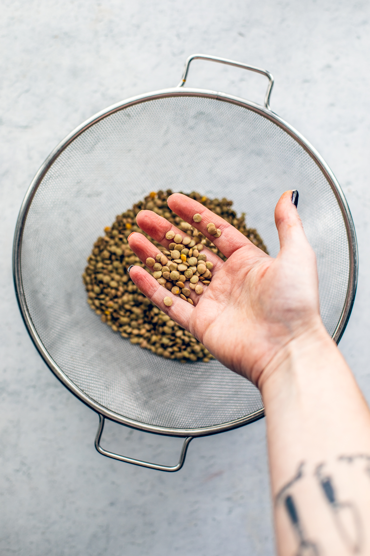 Hand sorting through lentils in colander.