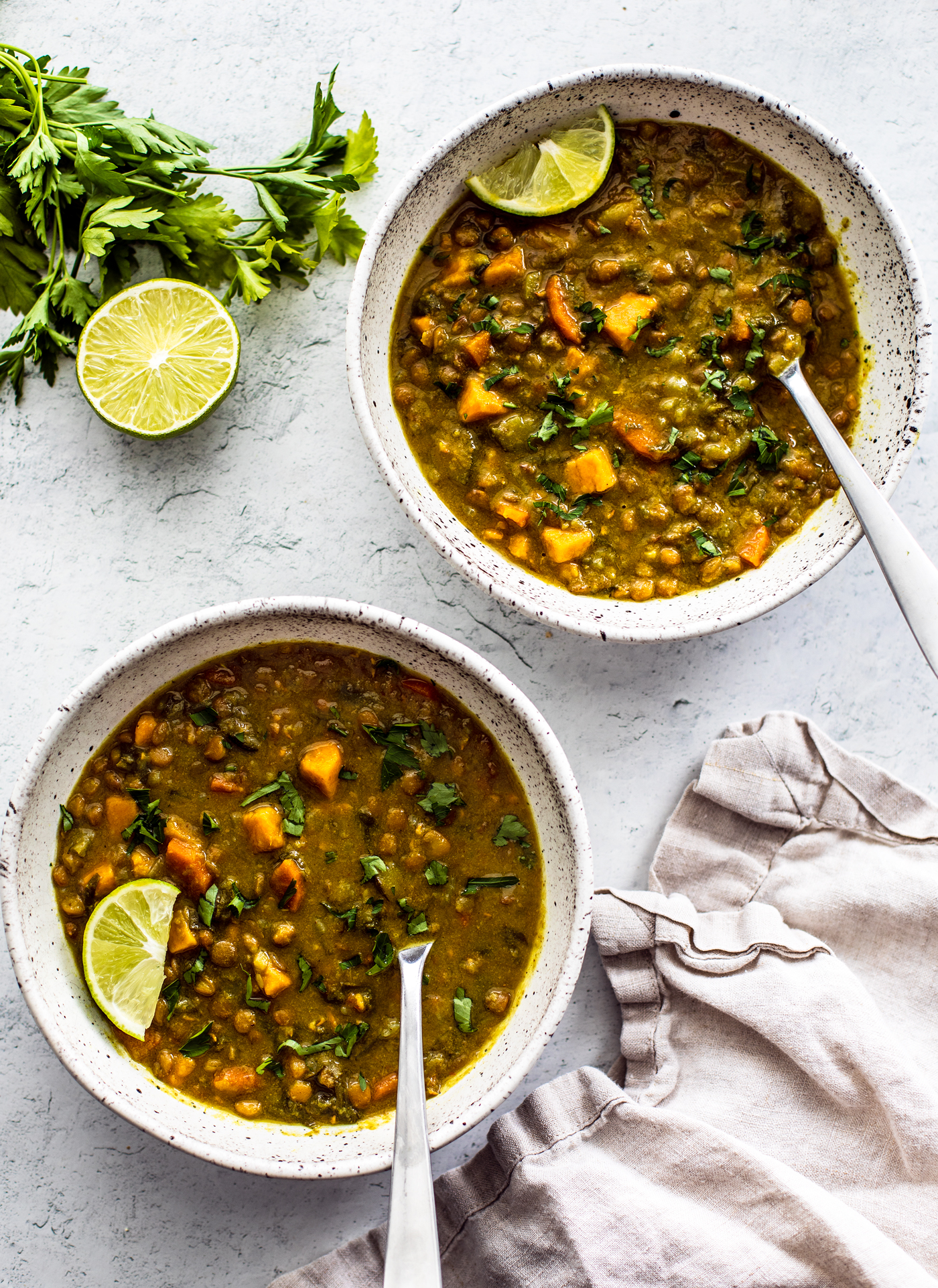 Two bowls of hearty lentil soup garnished with lime wedges.
