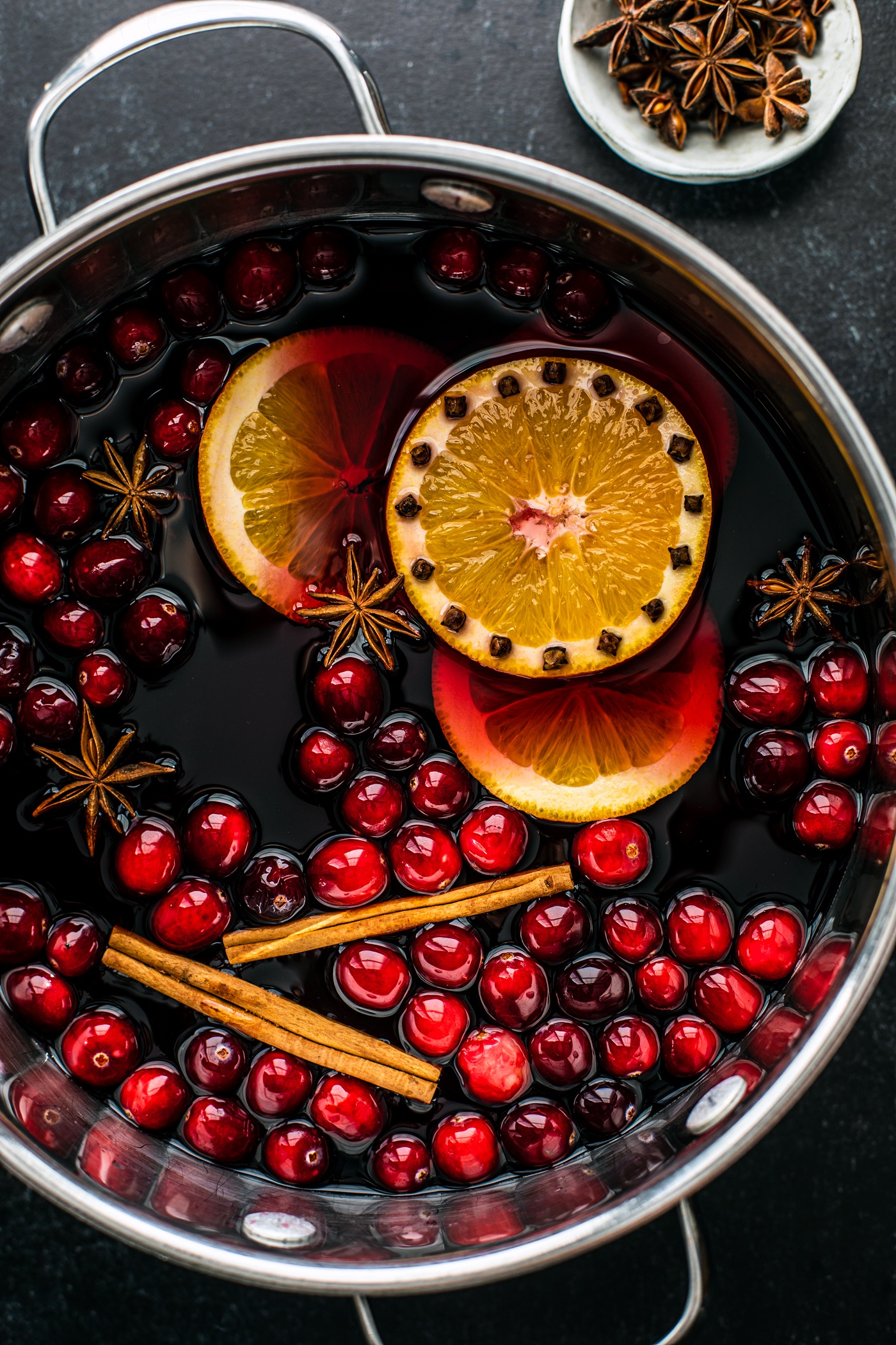 Large saucepan filled with mulled wine, cranberries, cinnamon sticks, orange slices, and star anise.