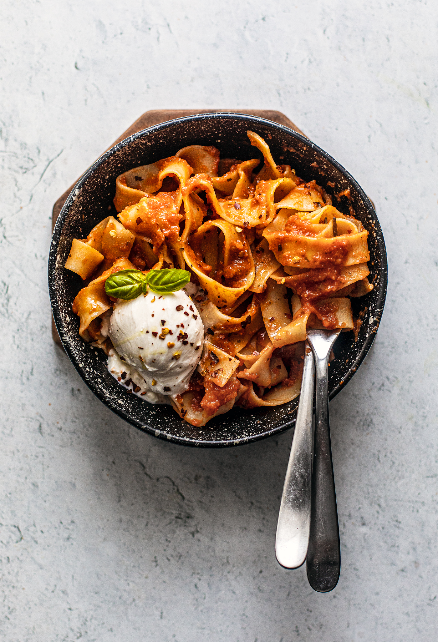 Black speckled bowl full of pappardelle and a scoop of burrata.