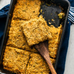 Cast iron casserole dish of broccoli casserole with a spatula scooping a portion.