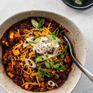 Turkey chili in a bowl with shredded cheddar, sour cream, and sliced scallions.
