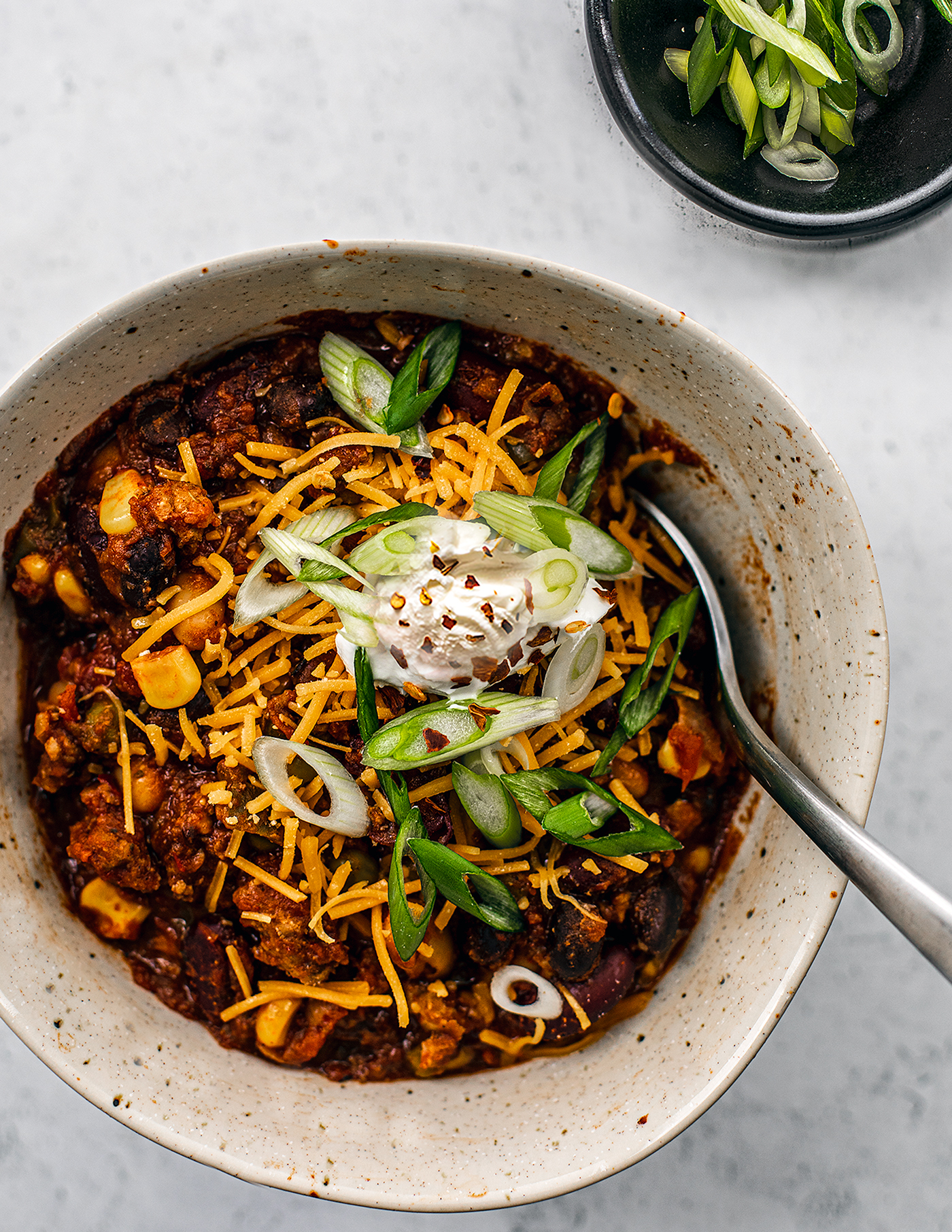 Turkey chili in a bowl with shredded cheddar, sour cream, and sliced scallions. 