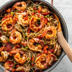 Close up of pan brimming with pasta and Cajun shrimp with a wooden serving spoon.