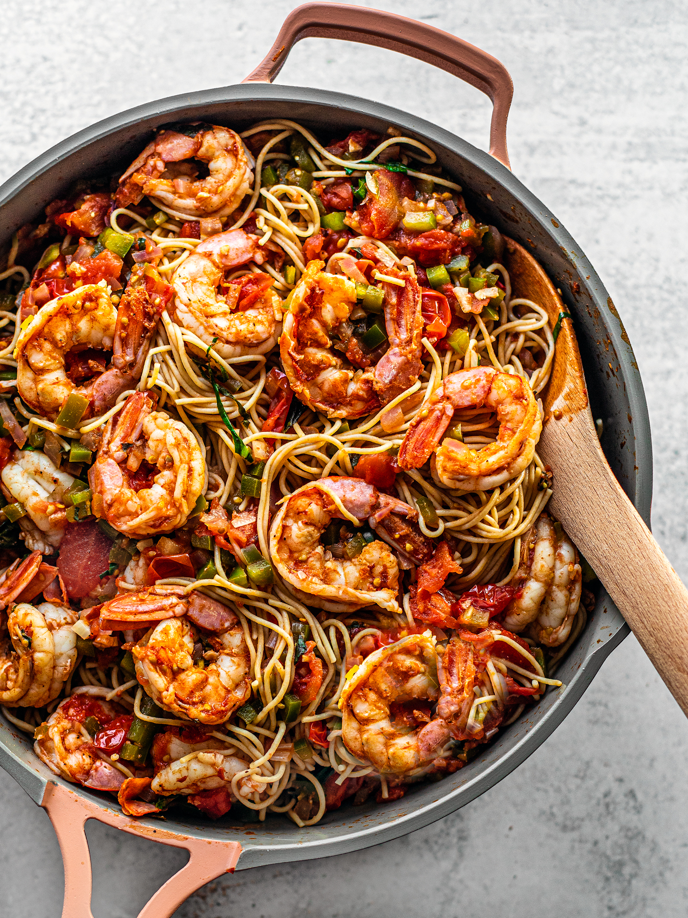 Close up of pan brimming with pasta and Cajun shrimp with a wooden serving spoon.