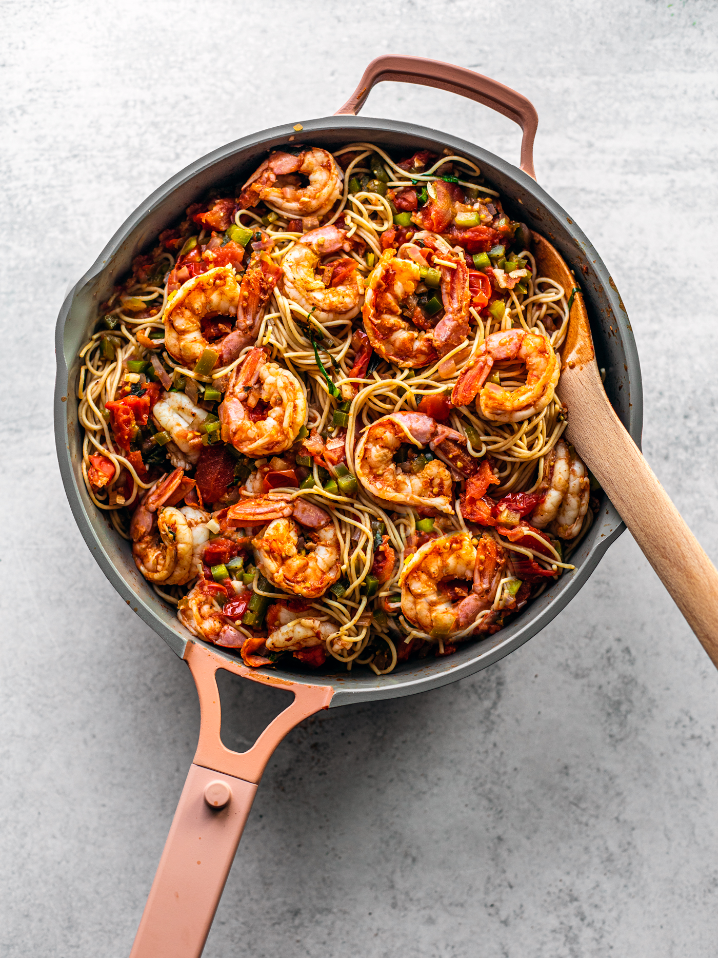 Pan brimming with pasta and Cajun shrimp with a wooden serving spoon.