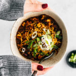 Hands with chunky-knit sweater holding a bowl of turkey chili.