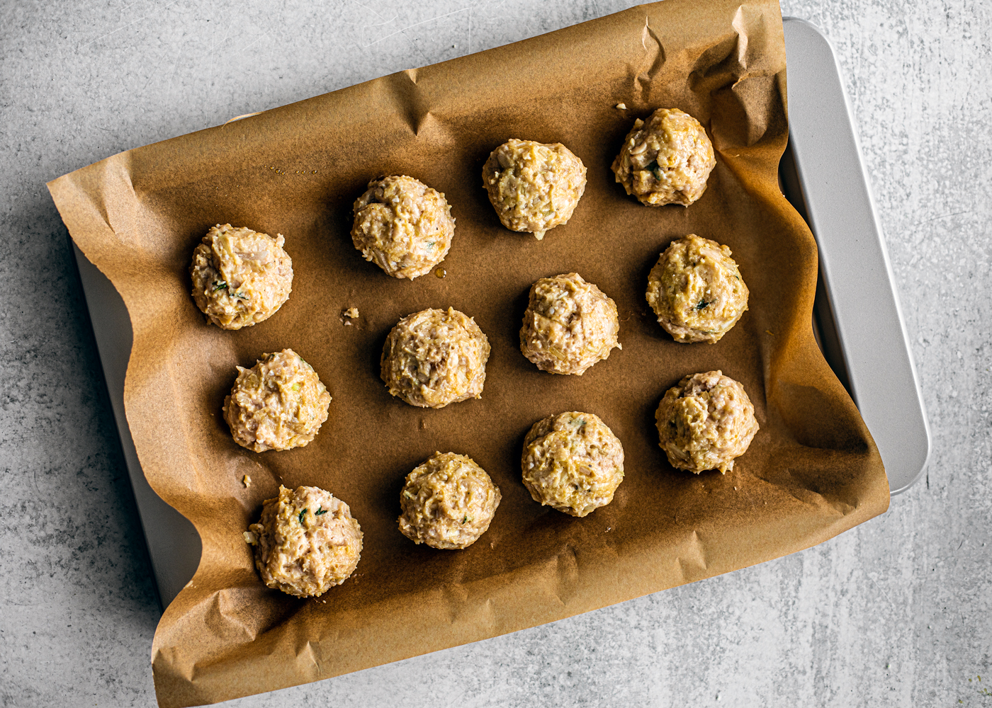 Baking sheet covered in parchment with raw chicken meatballs on top.