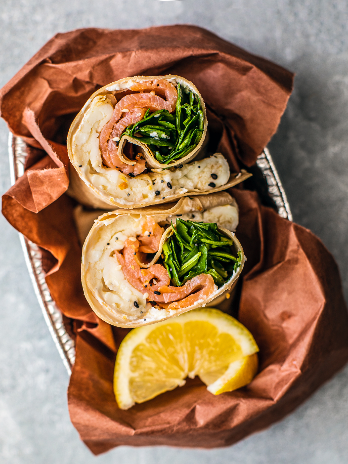 Smoked salmon wrap bundled in a serving tray with lemon wedges.