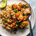 Plate with rice topped with cubed salmon tossed in sweet chili sauce and garnished with scallions and chilies.