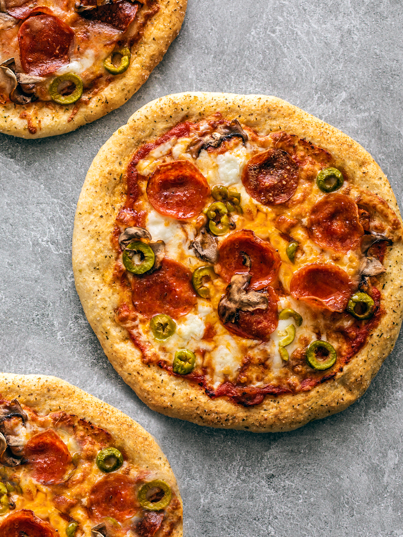 Golden pizzas topped with melted cheese, pepperoni, olives, and mushrooms.