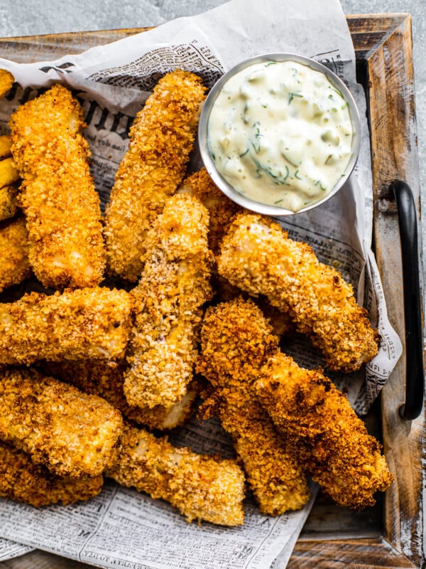 Close up of crispy golden fish sticks on platter with tartar sauce.
