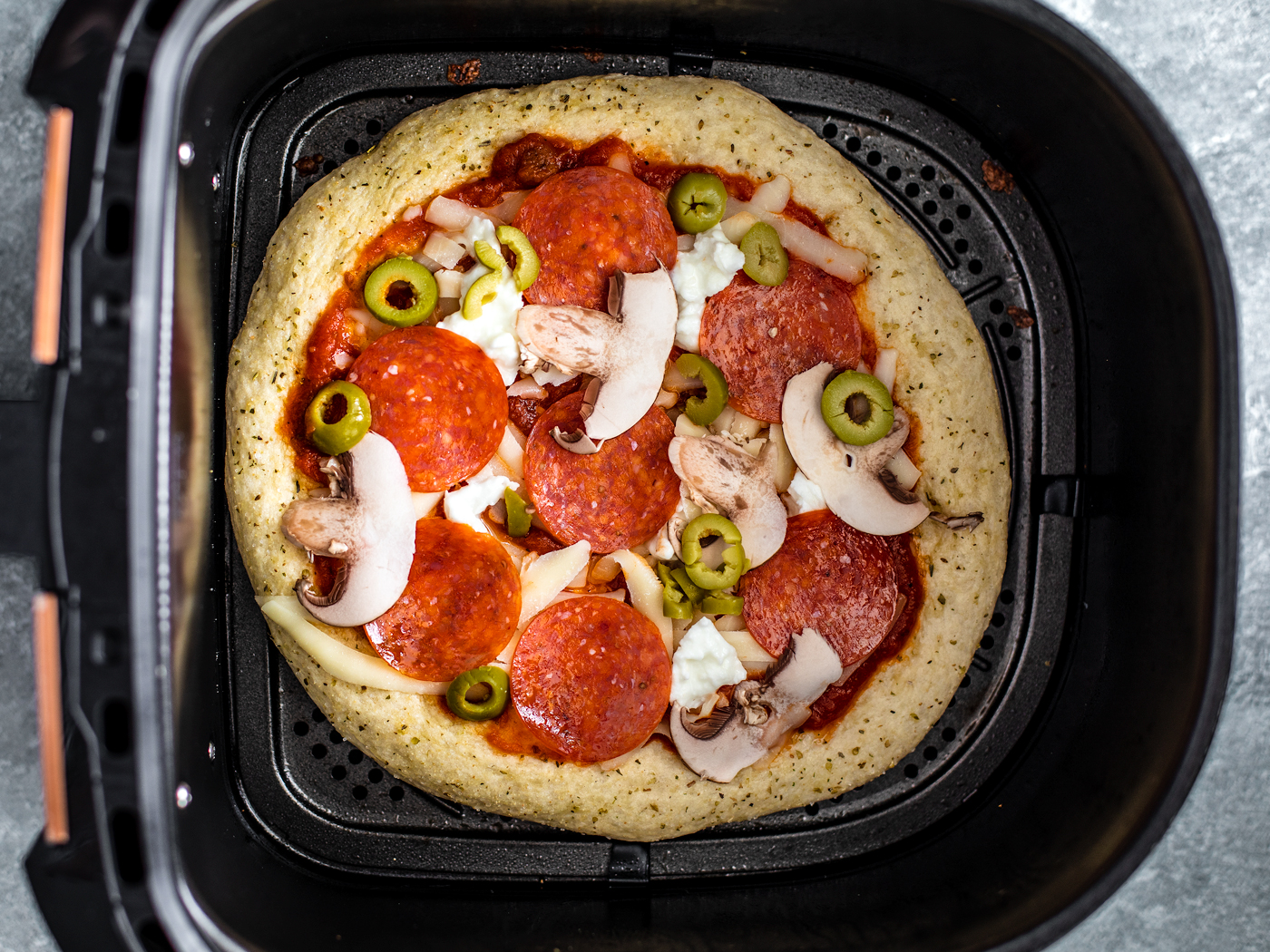 Uncooked pizza in air fryer basket.