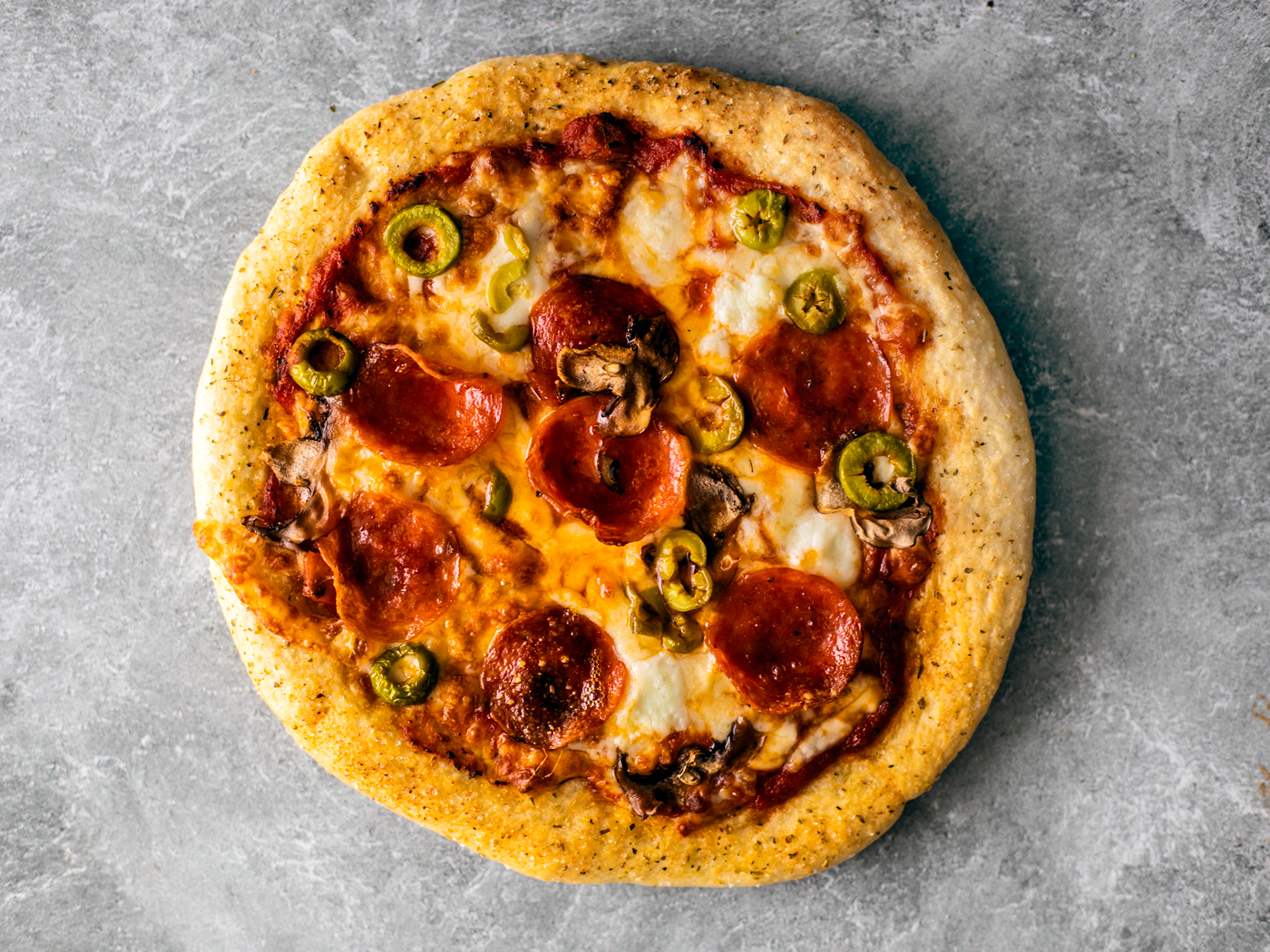 Golden crisp pizza with cheese, pepperoni, olives, and mushrooms.