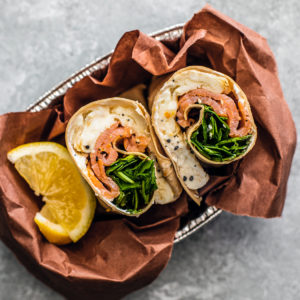Smoked salmon wrap bundled in a serving tray with lemon wedges.