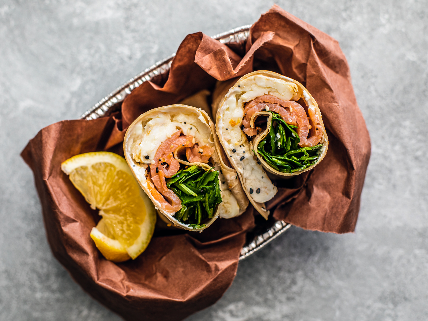 Smoked salmon wrap bundled in a serving tray with lemon wedges.
