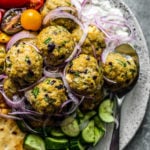 Close up of meatballs on a serving platter with tzatziki, fresh veggies, and pita.