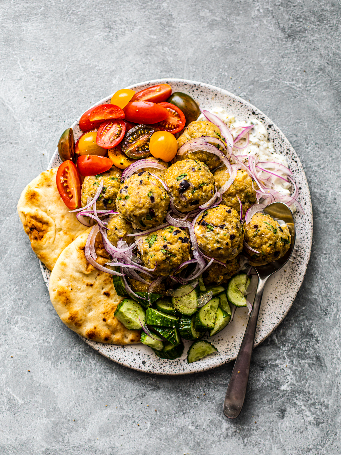 Meatballs on a serving platter with tzatziki, fresh veggies, and pita.