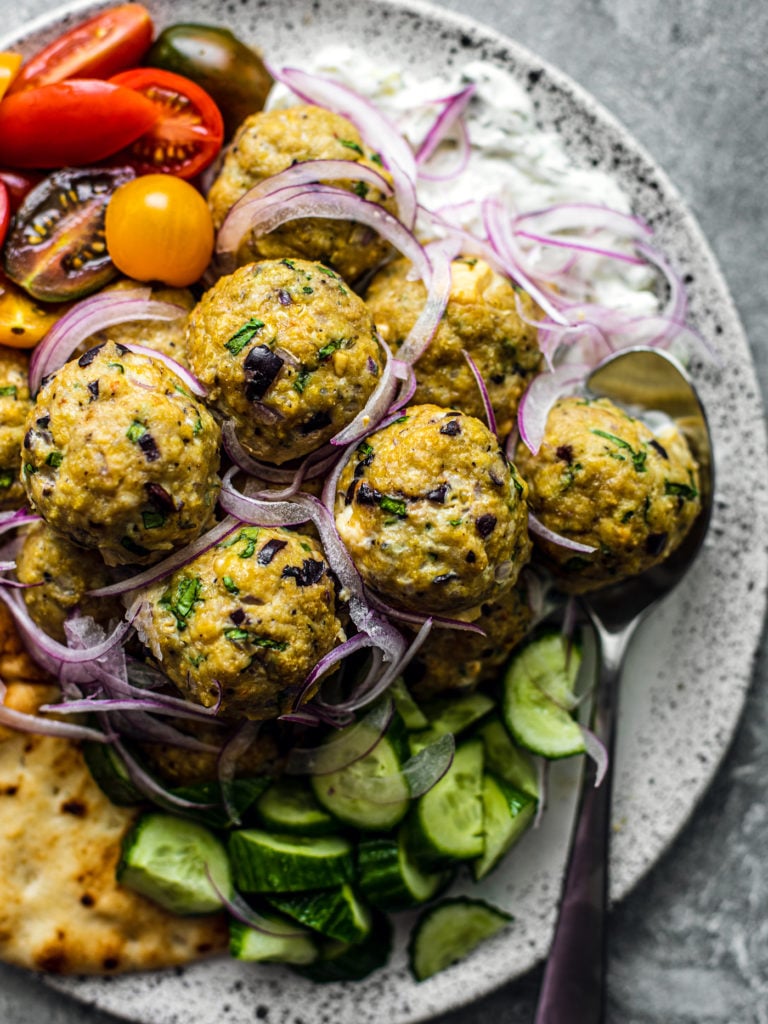 Close up of meatballs on a serving platter with tzatziki, fresh veggies, and pita.