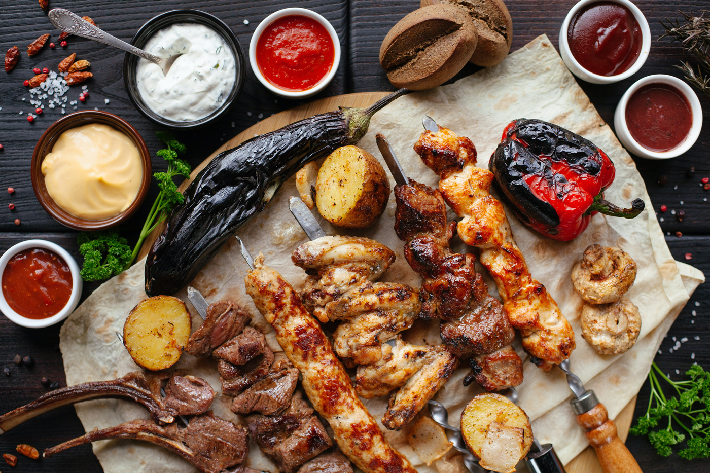 Grilled meats and vegetables on a platter with sauces on the side.