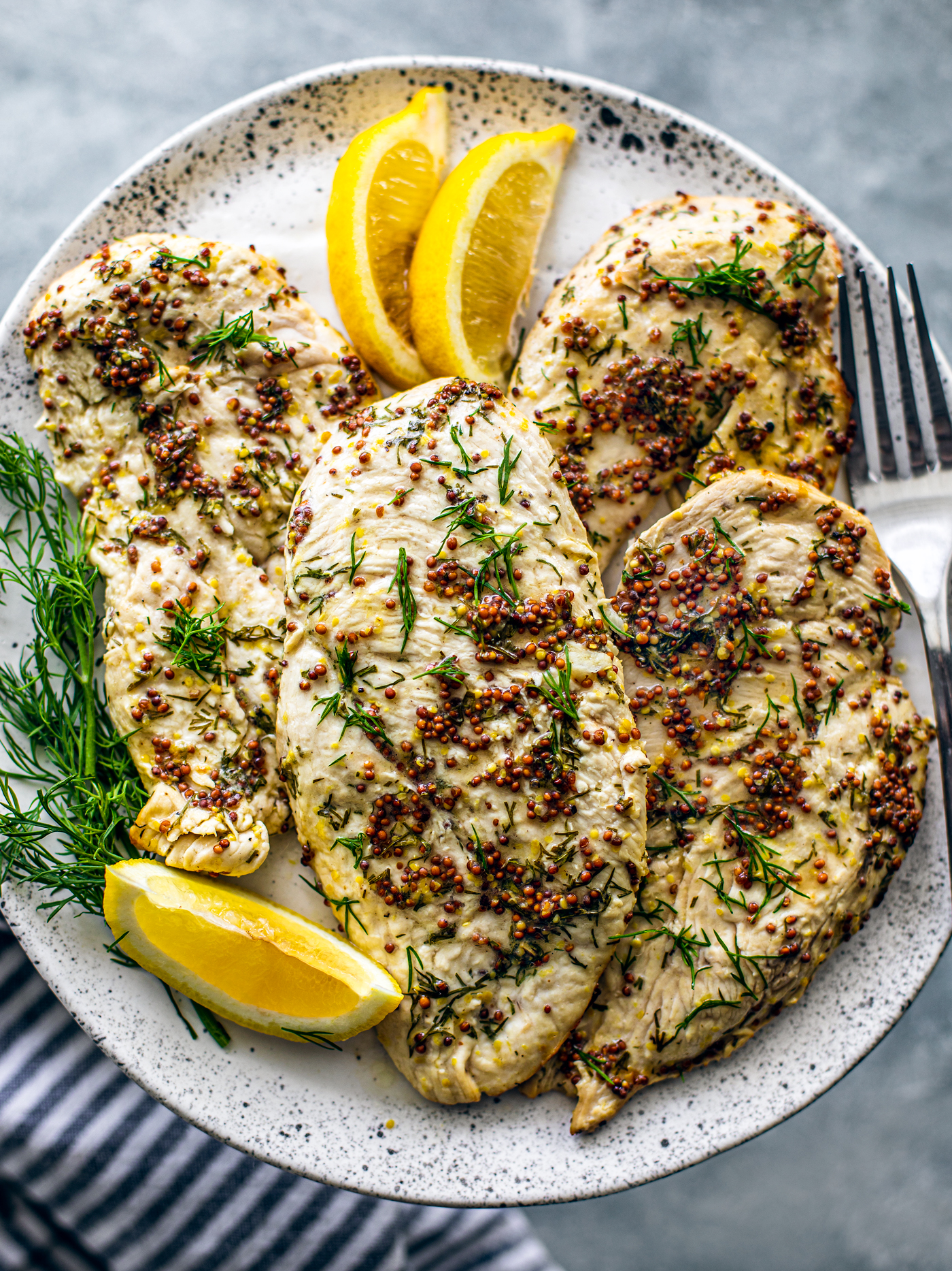 Plate of chicken breasts with lemon wedges and fresh dill sprigs.