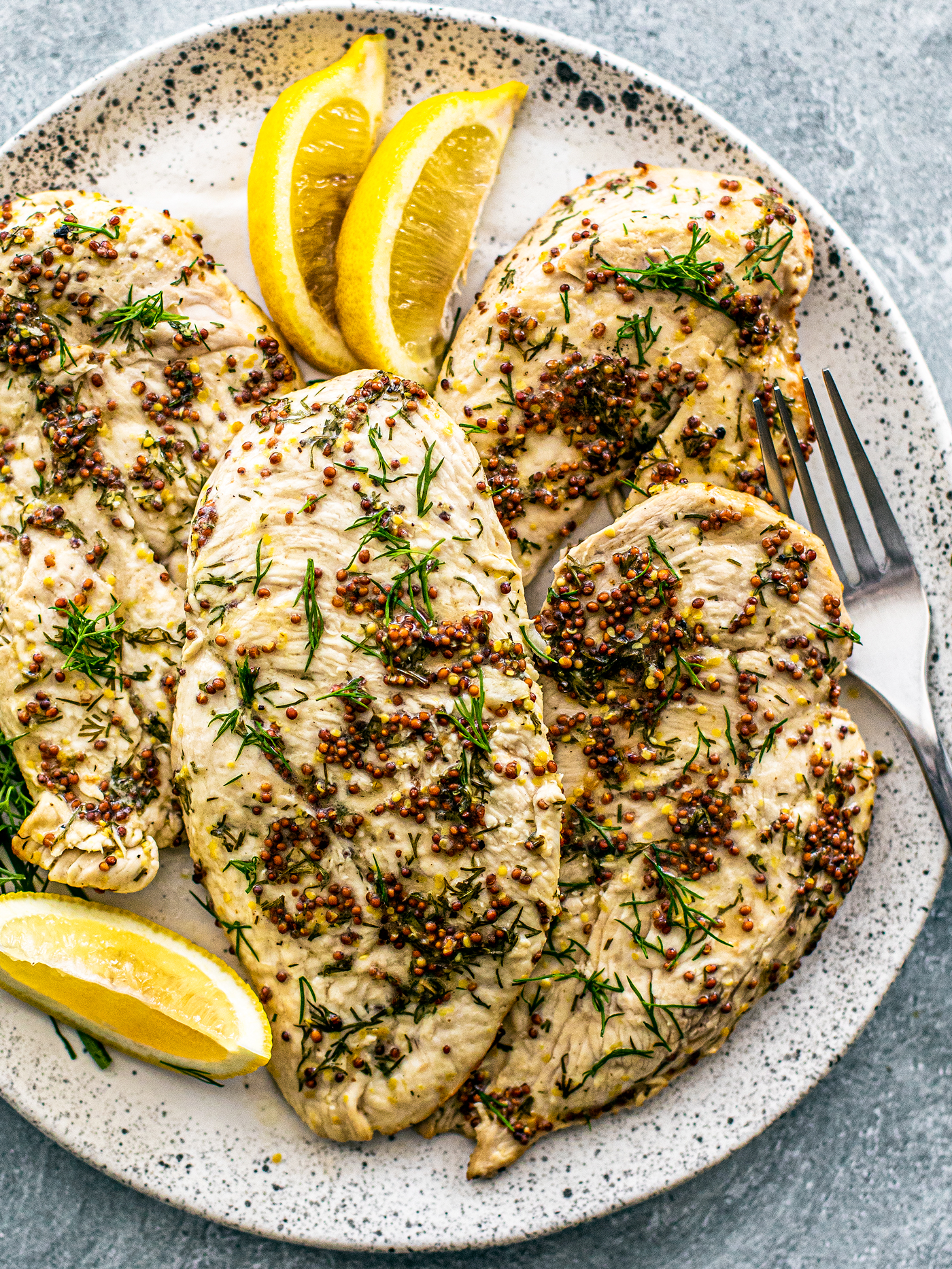 Plate of chicken breasts with lemon wedges and fresh dill sprigs.