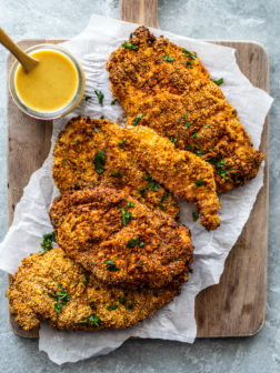 Wooden serving board with crispy chicken cutlets with honey mustard sauce on the side.