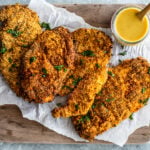 Wooden serving board with crispy chicken cutlets with honey mustard sauce on the side.