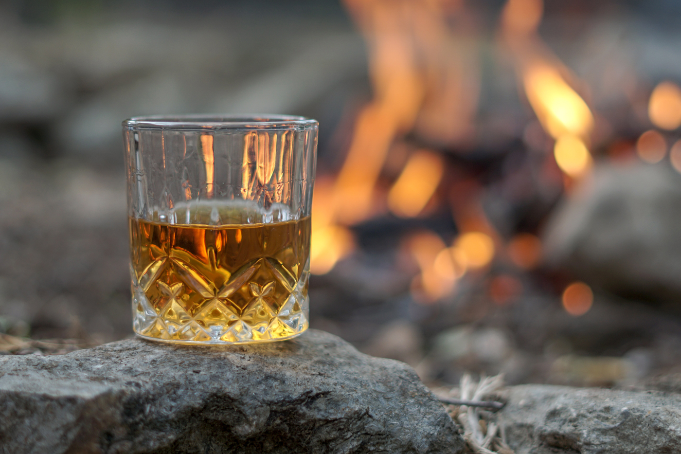 Glass of whiskey on a rock with fire in background.