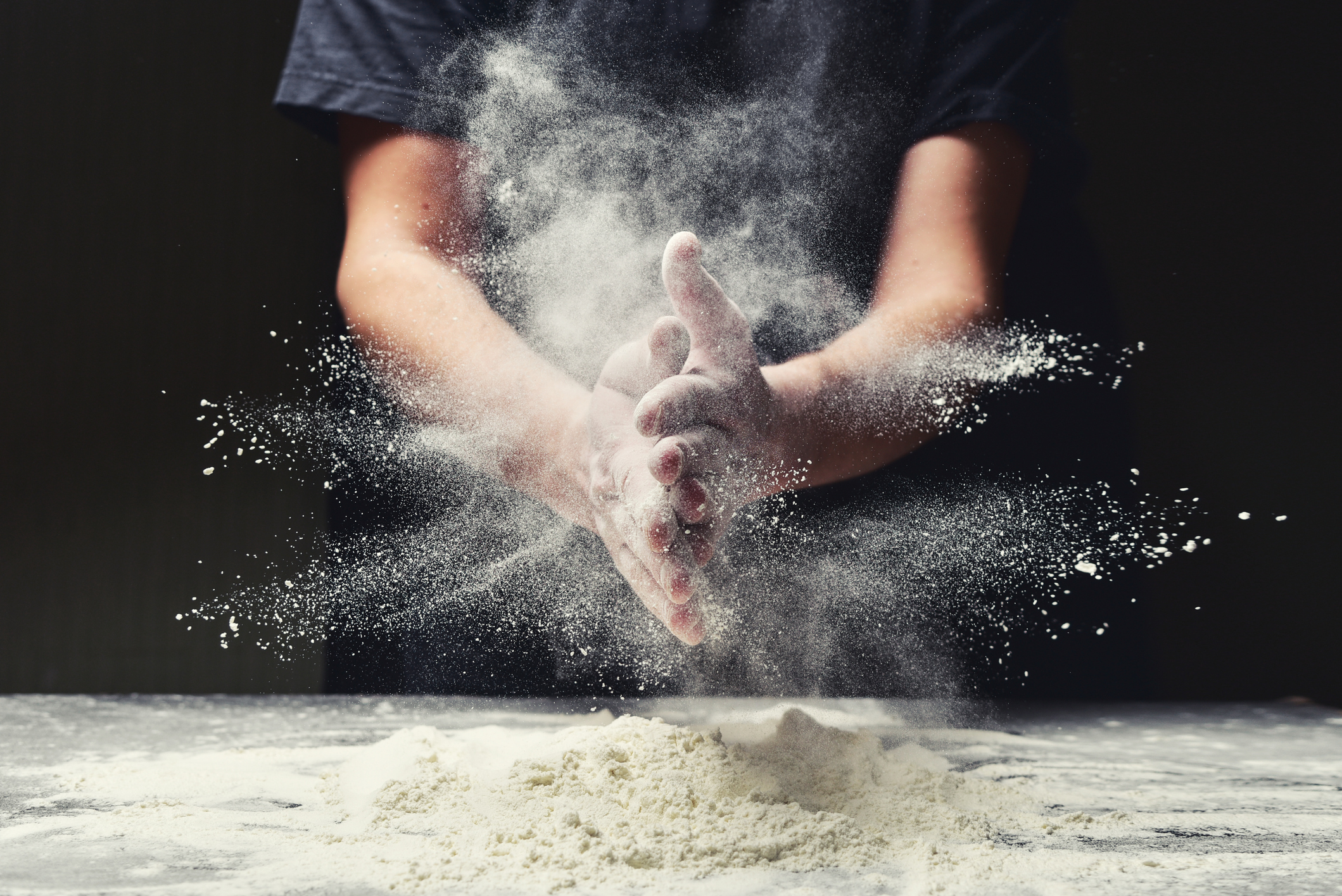 Hands clapping a cloud of flour over flour on a countertop.
