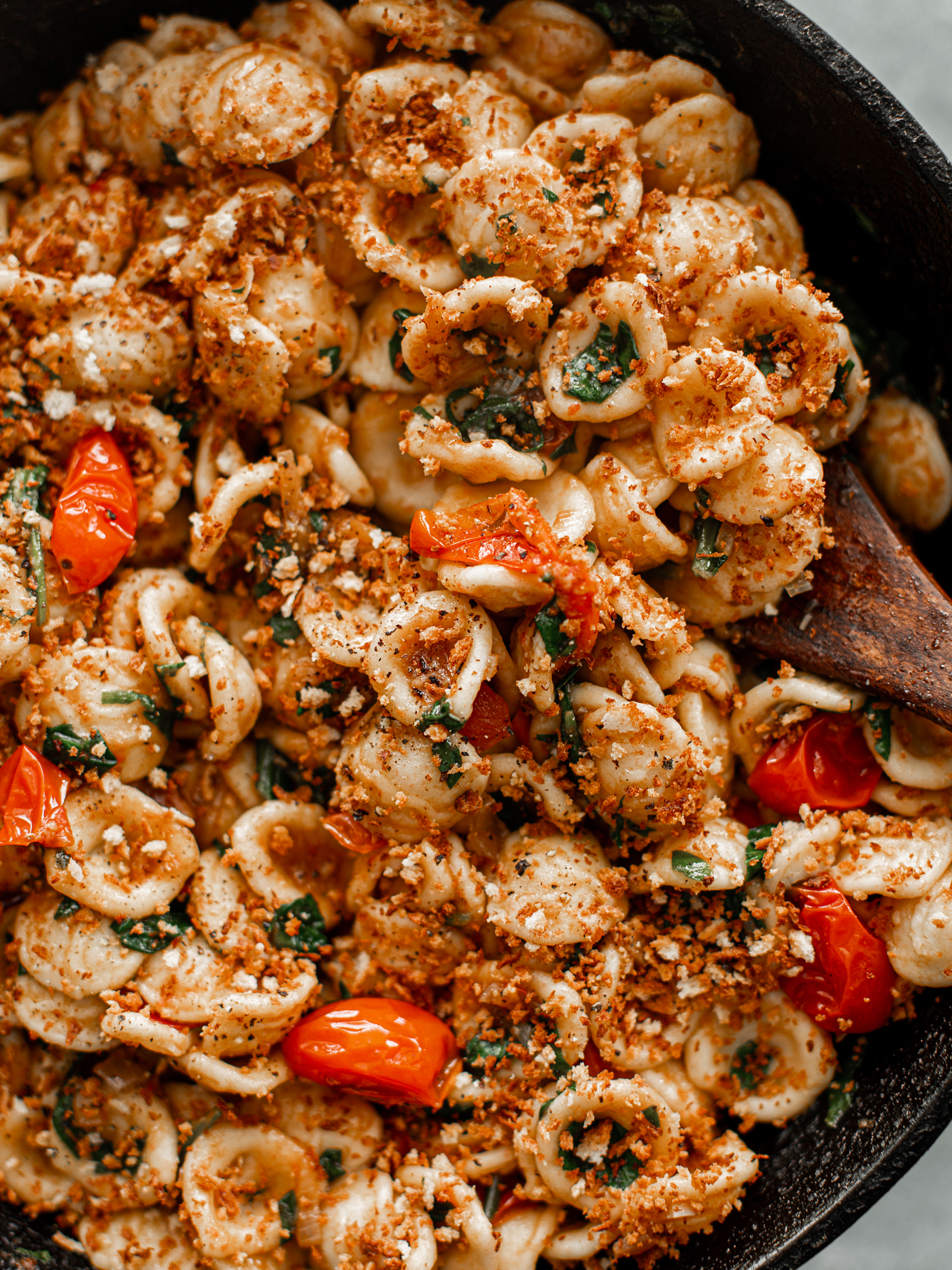 Close up of cooked orecchiette pasta with tomatoes, spinach, and breadcrumbs in a cast iron skillet.