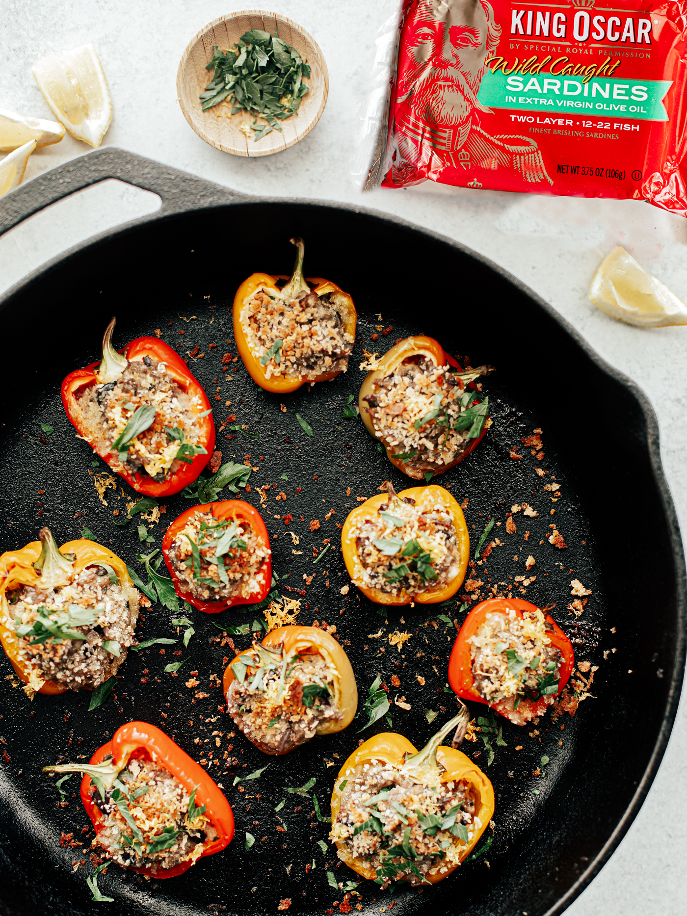 Cast iron pan with baked stuffed mini peppers covered in toasted breadcrumbs and tin of King Oscar sardines.