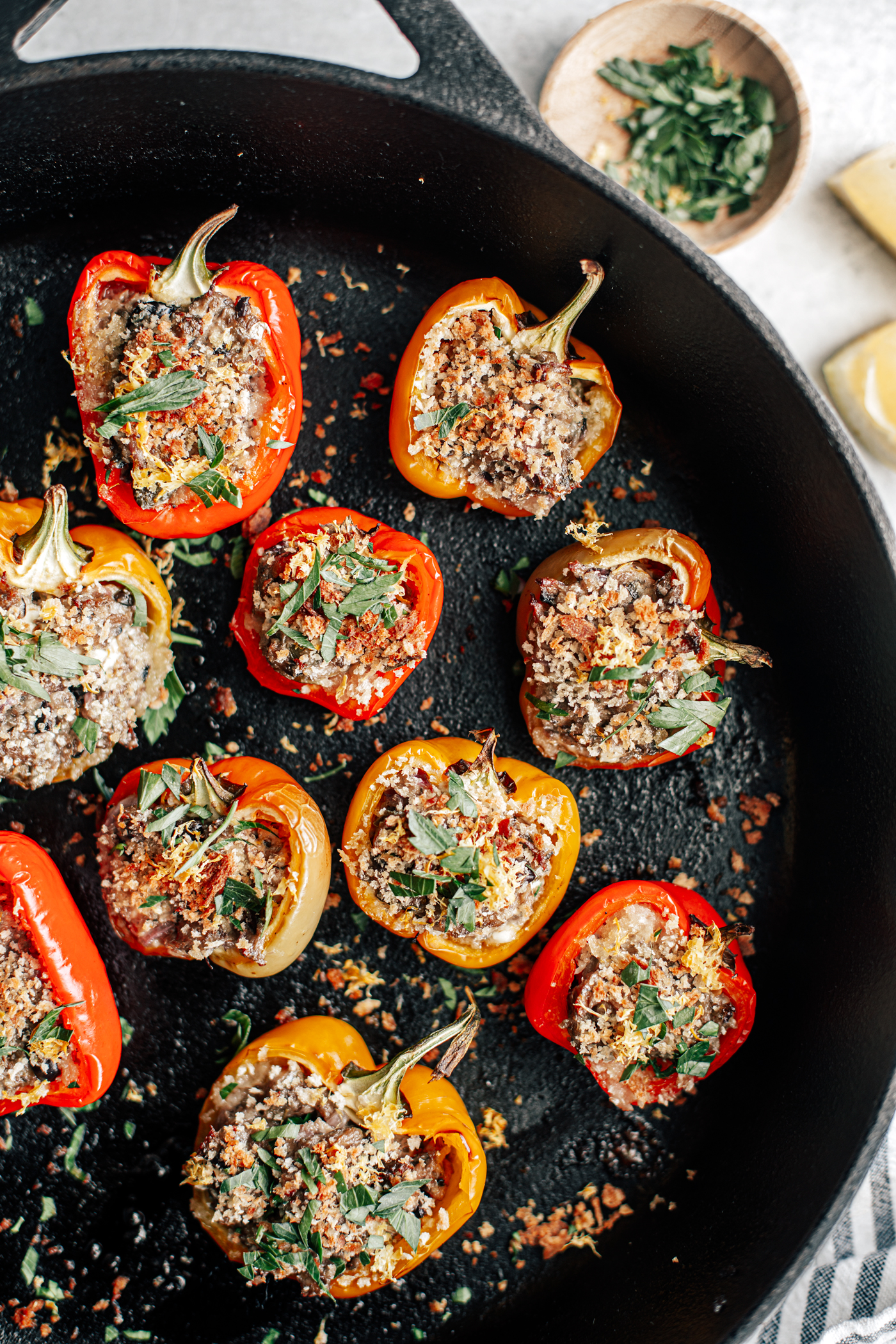 Cast iron pan with baked stuffed mini peppers covered in toasted breadcrumbs.