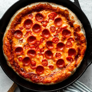 Cast iron pan with cheesy pepperoni pizza in it.