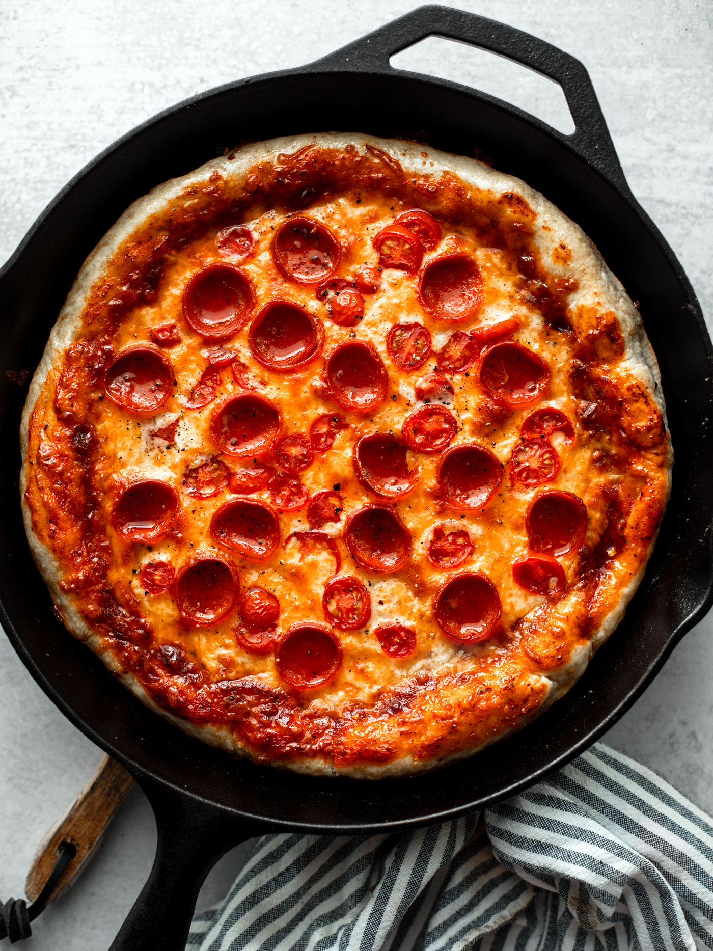 Cast iron pan with cheesy pepperoni pizza in it.