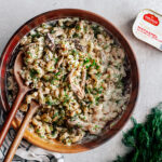 Bamboo serving bowl full of macaroni salad garnished with fresh dill, and a can of lemon mackerel on the side.