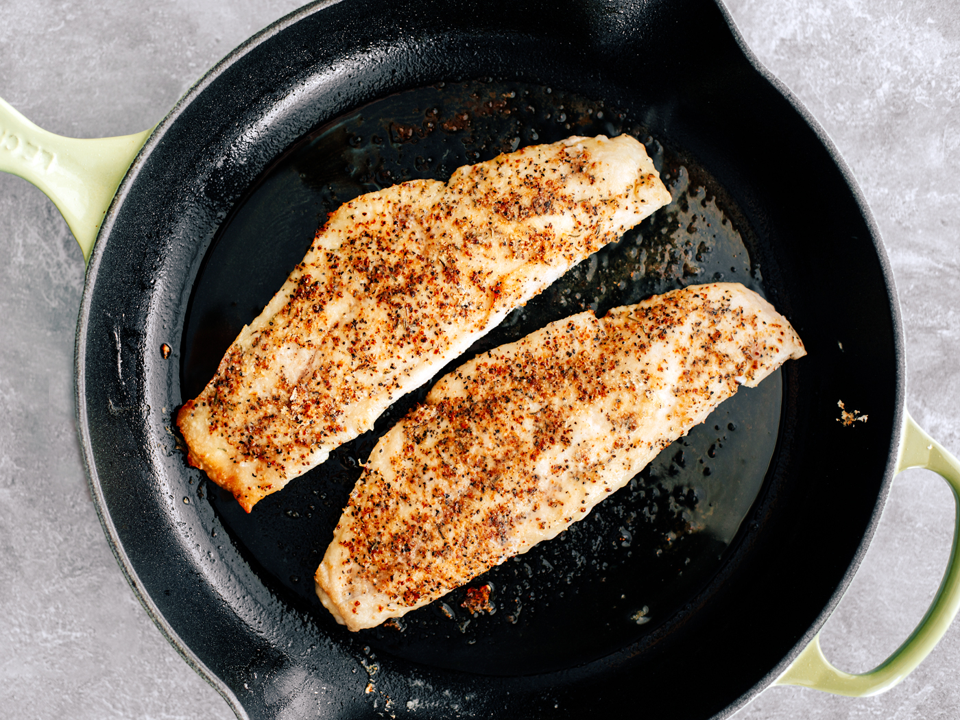 Skillet with seasoned and cooked grouper fillets in it.