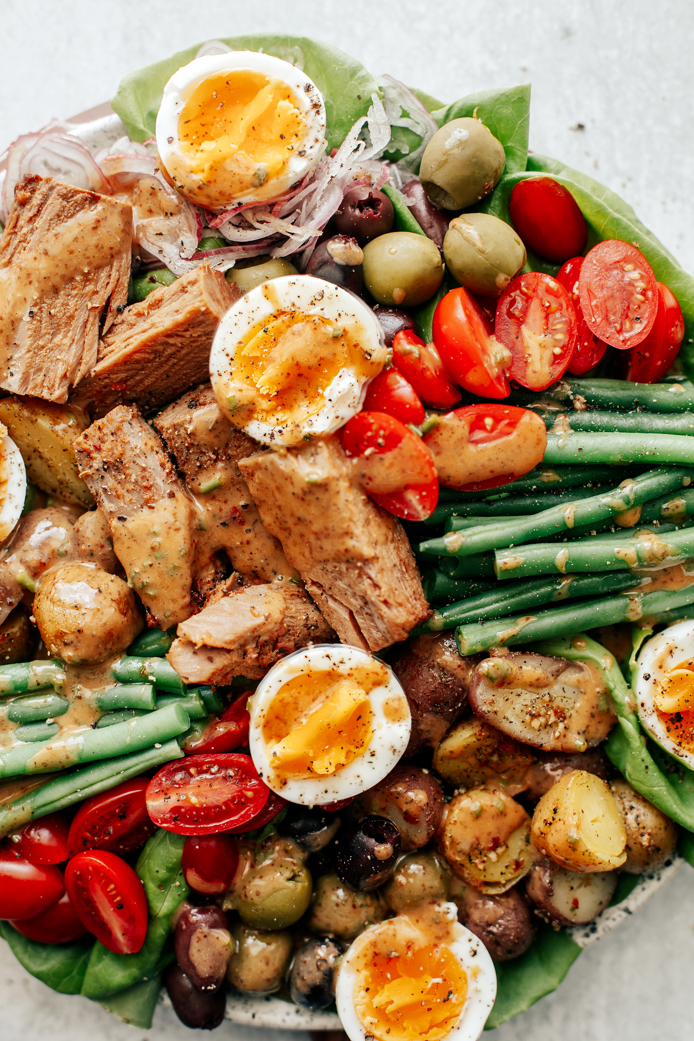 Close up of Niçoise salad with dressing drizzled over top.