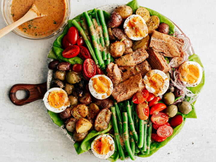 Colorful platter of Niçoise Salad with fresh veggie and soft-boiled egg with bowl of vinaigrette next to it.